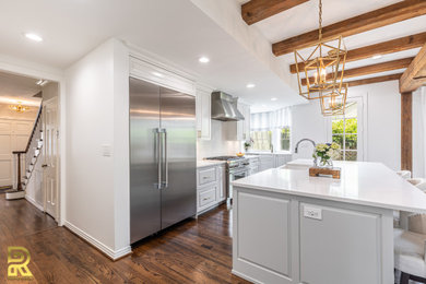 Inspiration for a large transitional medium tone wood floor open concept kitchen remodel in Dallas with a farmhouse sink, shaker cabinets, white cabinets, quartz countertops, white backsplash, quartz backsplash, stainless steel appliances, an island and white countertops