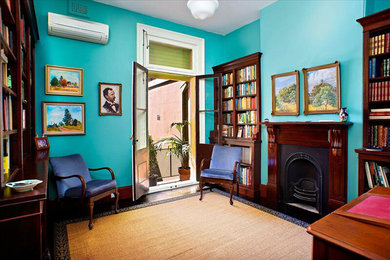 Photo of a mid-sized traditional enclosed living room in Sydney with a library, green walls, dark hardwood floors, a standard fireplace and a wood fireplace surround.