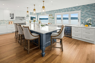 Inspiration for a large transitional u-shaped eat-in kitchen in Seattle with a farmhouse sink, recessed-panel cabinets, white cabinets, quartz benchtops, blue splashback, subway tile splashback, stainless steel appliances, medium hardwood floors, with island, brown floor and white benchtop.