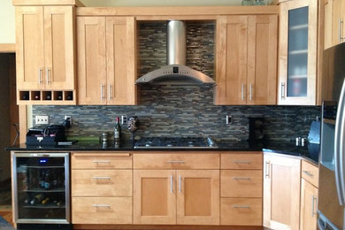 Mid-sized elegant l-shaped medium tone wood floor open concept kitchen photo in Other with recessed-panel cabinets, light wood cabinets, black backsplash, glass tile backsplash, stainless steel appliances and an island