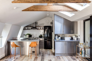 Inspiration for a small industrial galley kitchen in London with flat-panel cabinets, stainless steel cabinets, white splashback, subway tile splashback, black appliances and a peninsula.