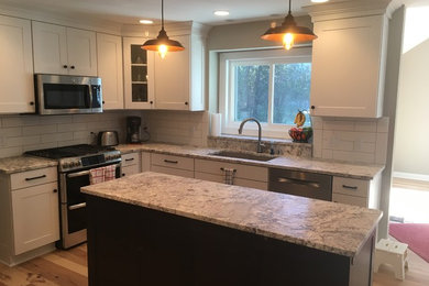 Example of a mid-sized classic l-shaped medium tone wood floor and brown floor eat-in kitchen design in Milwaukee with an undermount sink, recessed-panel cabinets, white cabinets, granite countertops, white backsplash, subway tile backsplash, stainless steel appliances and an island