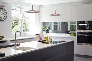 Design ideas for an expansive contemporary kitchen in Surrey with an integrated sink, flat-panel cabinets, grey cabinets, mirror splashback, black appliances, porcelain floors and with island.