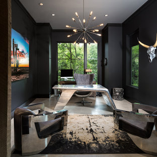 Bild på ett mellanstort industriellt hemmabibliotek, med svarta väggar, betonggolv och ett fristående skrivbord