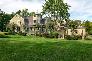 Large arts and crafts beige three-story concrete fiberboard and shingle house exterior photo in DC Metro with a gambrel roof, a mixed material roof and a brown roof