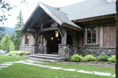 Modelo de fachada de casa gris rústica grande de tres plantas con revestimiento de piedra, tejado a dos aguas y tejado de teja de madera