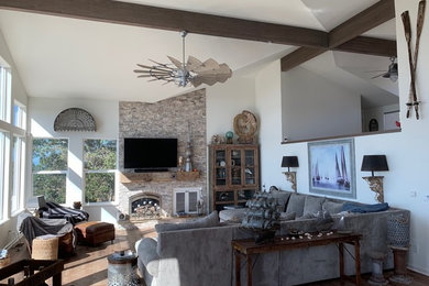 Example of a large beach style enclosed medium tone wood floor and brown floor family room design in San Luis Obispo with white walls, a standard fireplace, a stone fireplace and a wall-mounted tv