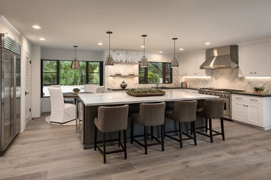 Large contemporary u-shaped kitchen in Santa Barbara with an undermount sink, shaker cabinets, white cabinets, marble benchtops, marble splashback, stainless steel appliances, light hardwood floors, grey floor, white splashback and with island.
