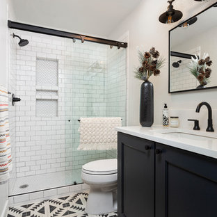 Réalisation d'une douche en alcôve tradition avec un placard à porte shaker, des portes de placard noires, un carrelage blanc, un carrelage métro, un mur blanc, un lavabo encastré, un sol multicolore, une cabine de douche à porte coulissante et un plan de toilette blanc.