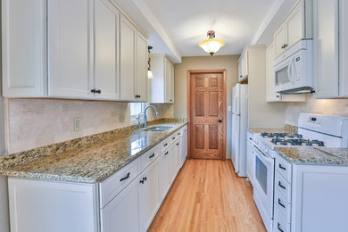 Inspiration for a small transitional galley light wood floor enclosed kitchen remodel in Minneapolis with a double-bowl sink, shaker cabinets, white cabinets, granite countertops, beige backsplash, ceramic backsplash, white appliances and no island