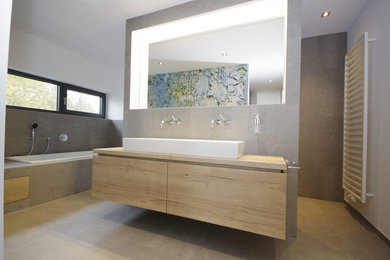 Großes Modernes Badezimmer En Suite mit flächenbündigen Schrankfronten, braunen Schränken, Einbaubadewanne, bodengleicher Dusche, Wandtoilette, grauer Wandfarbe, Zementfliesen für Boden, Aufsatzwaschbecken, Waschtisch aus Holz, braunem Boden, offener Dusche und brauner Waschtischplatte in Sonstige