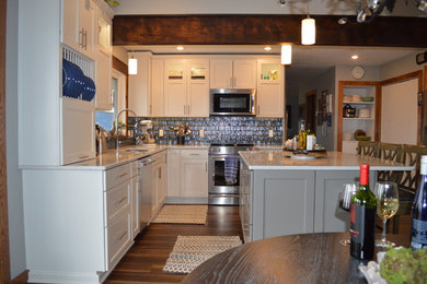Inspiration for a mid-sized transitional l-shaped brown floor eat-in kitchen remodel in Other with a double-bowl sink, shaker cabinets, white cabinets, quartzite countertops, multicolored backsplash, glass tile backsplash, stainless steel appliances, an island and white countertops