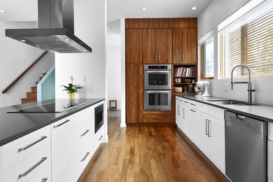 Example of a mid-sized minimalist galley medium tone wood floor and brown floor open concept kitchen design in Edmonton with flat-panel cabinets, stainless steel appliances, an undermount sink, white cabinets, solid surface countertops and a peninsula