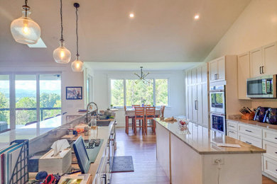 Open concept kitchen - large cottage single-wall medium tone wood floor, brown floor and vaulted ceiling open concept kitchen idea in Other with shaker cabinets, white cabinets, quartzite countertops, gray backsplash, stainless steel appliances, two islands and gray countertops