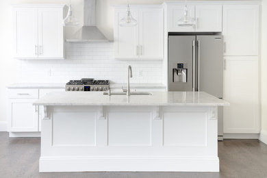 Kitchen - large transitional single-wall dark wood floor and brown floor kitchen idea in New York with an undermount sink, shaker cabinets, white cabinets, quartz countertops, white backsplash, subway tile backsplash, stainless steel appliances and an island
