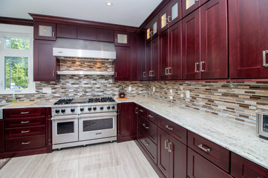 Photo of an expansive transitional l-shaped eat-in kitchen in Boston with a farmhouse sink, recessed-panel cabinets, medium wood cabinets, granite benchtops, multi-coloured splashback, glass tile splashback, stainless steel appliances, porcelain floors, with island, beige floor and multi-coloured benchtop.