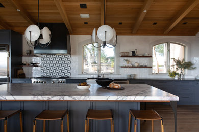 Example of a transitional galley medium tone wood floor, brown floor, exposed beam, vaulted ceiling and wood ceiling kitchen design in San Francisco with a farmhouse sink, shaker cabinets, blue cabinets, white backsplash, stainless steel appliances, an island and white countertops
