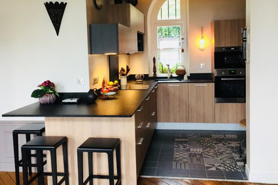 Exemple d'une cuisine ouverte tendance en L et bois clair de taille moyenne avec un évier 1 bac, un plan de travail en granite, une crédence noire, un électroménager en acier inoxydable, un sol en carrelage de céramique et un sol noir.
