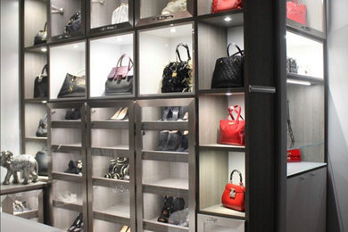 Example of a large danish women's marble floor and beige floor walk-in closet design in Miami with glass-front cabinets and light wood cabinets
