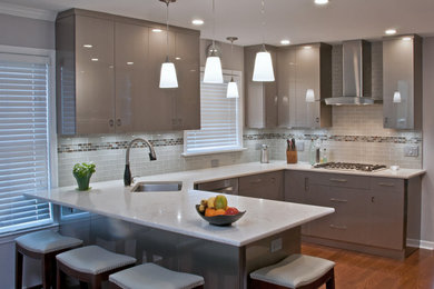 Mid-sized trendy u-shaped medium tone wood floor and brown floor eat-in kitchen photo in Chicago with an undermount sink, flat-panel cabinets, quartz countertops, glass tile backsplash, stainless steel appliances, a peninsula, gray backsplash and gray cabinets