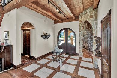 Example of a large trendy medium tone wood floor, multicolored floor and exposed beam entryway design in Houston with white walls and a dark wood front door