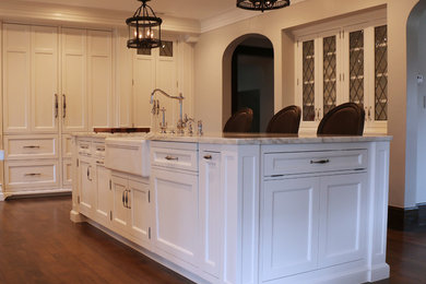 Eat-in kitchen - large traditional l-shaped medium tone wood floor eat-in kitchen idea in Detroit with a farmhouse sink, recessed-panel cabinets, white cabinets, marble countertops, white backsplash, stone slab backsplash, paneled appliances and an island