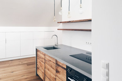 Offene, Einzeilige, Mittelgroße Moderne Küche mit integriertem Waschbecken, flächenbündigen Schrankfronten, hellbraunen Holzschränken, Betonarbeitsplatte, Küchenrückwand in Weiß, schwarzen Elektrogeräten und braunem Holzboden in Berlin