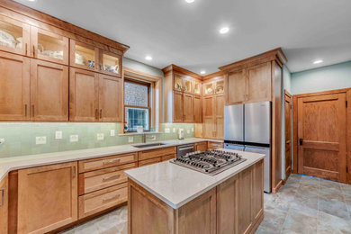 Example of a mid-sized arts and crafts u-shaped porcelain tile and multicolored floor eat-in kitchen design in St Louis with a single-bowl sink, shaker cabinets, medium tone wood cabinets, quartz countertops, green backsplash, ceramic backsplash, stainless steel appliances, an island and beige countertops