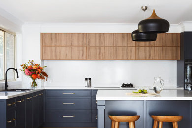 Inspiration for an expansive transitional l-shaped open plan kitchen in Sydney with a double-bowl sink, shaker cabinets, blue cabinets, quartz benchtops, white splashback, engineered quartz splashback, black appliances, laminate floors, with island, brown floor and white benchtop.