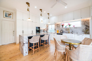 Photo of a mid-sized l-shaped open plan kitchen in Sydney with a farmhouse sink, brown splashback, marble splashback, black appliances, dark hardwood floors, with island, brown floor and brown benchtop.