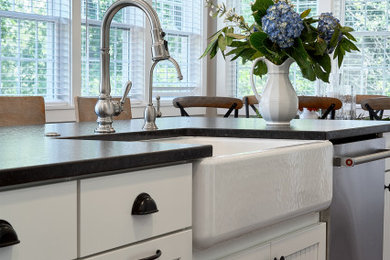 Example of a mid-sized country galley medium tone wood floor and brown floor open concept kitchen design in Chicago with a farmhouse sink, shaker cabinets, white cabinets, granite countertops, white backsplash, ceramic backsplash, stainless steel appliances, an island and black countertops
