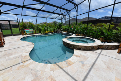 Photo of an expansive beach style backyard custom-shaped natural pool in Orlando with a hot tub and natural stone pavers.