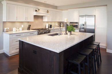 Photo of a mid-sized transitional l-shaped kitchen in Calgary with a double-bowl sink, shaker cabinets, white cabinets, granite benchtops, stainless steel appliances, dark hardwood floors, with island and brown floor.