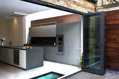 Photo of a large contemporary single-wall eat-in kitchen in London with an integrated sink, glass-front cabinets, grey cabinets, brown splashback, timber splashback, stainless steel appliances, porcelain floors, with island, grey floor and grey benchtop.