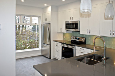 Mid-sized minimalist l-shaped ceramic tile and black floor open concept kitchen photo in Vancouver with a double-bowl sink, shaker cabinets, white cabinets, solid surface countertops, green backsplash, glass tile backsplash, stainless steel appliances and a peninsula