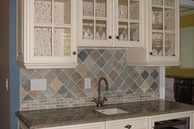 Open concept kitchen - large traditional u-shaped dark wood floor open concept kitchen idea in New York with an undermount sink, glass-front cabinets, yellow cabinets, granite countertops, multicolored backsplash, ceramic backsplash, stainless steel appliances and an island