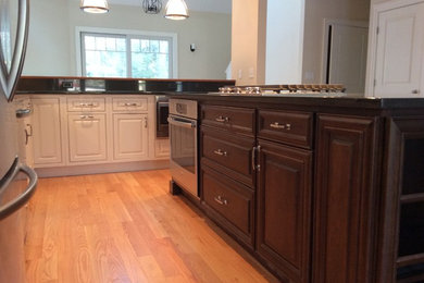 Inspiration for a mid-sized transitional l-shaped light wood floor, brown floor and vaulted ceiling kitchen pantry remodel in Boston with an undermount sink, raised-panel cabinets, dark wood cabinets, granite countertops, stainless steel appliances, an island and black countertops