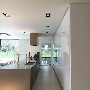 Foto de cocina lineal, contemporánea, grande, abierta, con fregadero de doble seno, armarios con paneles lisos, puertas de armario blancas, electrodomésticos negros, suelo de azulejos de cemento, una isla y suelo gris