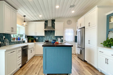 Inspiration for a mid-sized farmhouse l-shaped laminate floor, brown floor and vaulted ceiling open concept kitchen remodel in Los Angeles with a farmhouse sink, raised-panel cabinets, white cabinets, quartz countertops, blue backsplash, ceramic backsplash, stainless steel appliances, an island and white countertops