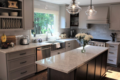 Example of a large transitional galley medium tone wood floor and brown floor eat-in kitchen design in Detroit with a farmhouse sink, shaker cabinets, gray cabinets, quartz countertops, gray backsplash, ceramic backsplash, stainless steel appliances, an island and gray countertops