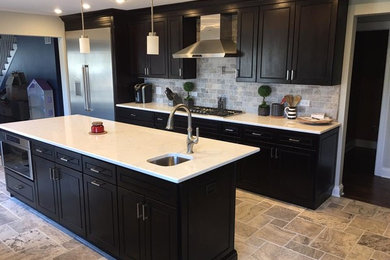 Inspiration for a large transitional l-shaped porcelain tile and beige floor kitchen remodel in Chicago with an undermount sink, beaded inset cabinets, black cabinets, solid surface countertops, gray backsplash, stone tile backsplash, stainless steel appliances and an island