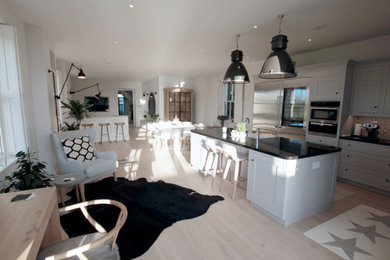 Diseño de cocina comedor contemporánea con armarios estilo shaker, salpicadero con mosaicos de azulejos, suelo de madera clara, una isla, encimeras negras y puertas de armario blancas