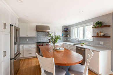 Example of a mid-sized transitional u-shaped light wood floor and brown floor eat-in kitchen design in Boston with an undermount sink, shaker cabinets, white cabinets, quartz countertops, gray backsplash, ceramic backsplash, stainless steel appliances, an island and gray countertops