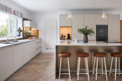 Inspiration for a large contemporary l-shaped kitchen/diner in Wiltshire with a built-in sink, flat-panel cabinets, white cabinets, engineered stone countertops, medium hardwood flooring and an island.
