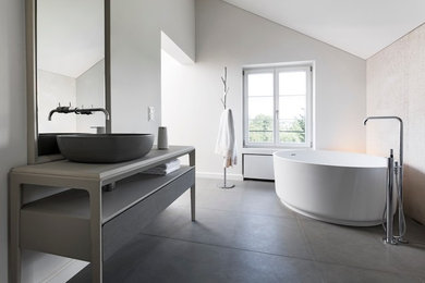 Großes Modernes Badezimmer En Suite mit flächenbündigen Schrankfronten, grauen Schränken, freistehender Badewanne, bodengleicher Dusche, Wandtoilette mit Spülkasten, beigen Fliesen, Kalkfliesen, weißer Wandfarbe, Kalkstein, Aufsatzwaschbecken, grauem Boden, Schiebetür-Duschabtrennung und beiger Waschtischplatte in Stuttgart