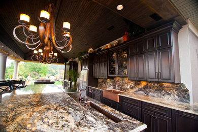 Large tuscan galley concrete floor eat-in kitchen photo in Other with a farmhouse sink, recessed-panel cabinets, dark wood cabinets, granite countertops, stone slab backsplash, stainless steel appliances and two islands