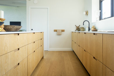 Large scandi l-shaped open plan kitchen in Other with a double-bowl sink, flat-panel cabinets, light wood cabinets, marble worktops, black appliances, an island and beige worktops.