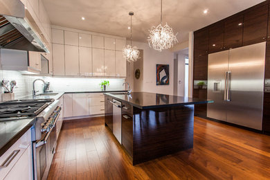 Inspiration for a large contemporary l-shaped medium tone wood floor kitchen remodel in Toronto with an undermount sink, flat-panel cabinets, white cabinets, solid surface countertops, white backsplash, glass tile backsplash, stainless steel appliances and an island
