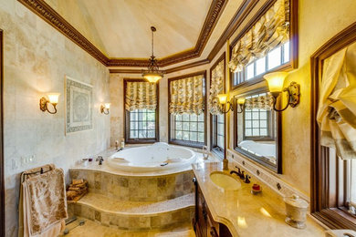 Photo of a mid-sized traditional master bathroom in Detroit with recessed-panel cabinets, dark wood cabinets, a drop-in tub, beige tile, mosaic tile, beige walls, travertine floors, an undermount sink, marble benchtops, beige floor, a corner shower and a hinged shower door.