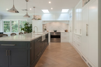 This is an example of an expansive traditional l-shaped eat-in kitchen in Sydney with a farmhouse sink, shaker cabinets, white cabinets, quartz benchtops, white splashback, marble splashback, stainless steel appliances, light hardwood floors, with island and white benchtop.